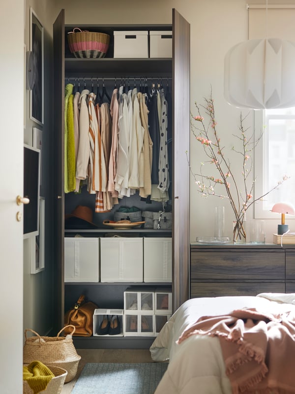 A grey/dark brown PAX/STORKLINTA wardrobe with the doors open showing clothes hanging on a rail and storage boxes on shelves.