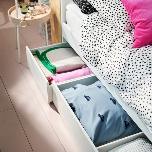 A white VIHALs double bed covered in BJÖRKGRÅMAL bed linen with two storage drawers open holding folded bed linen.