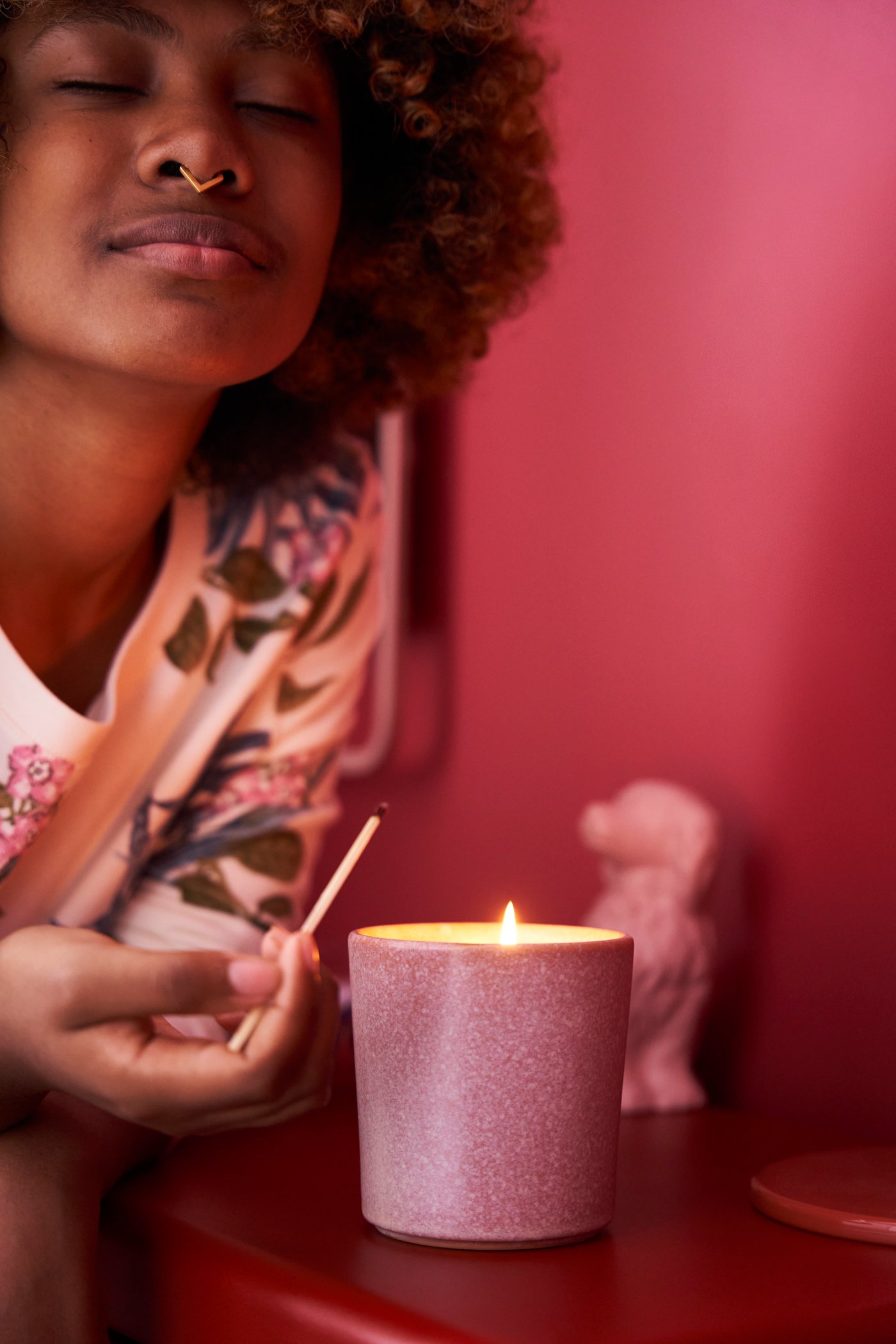 En person luktar på ett jasmin/rosa LUGNARE doftljus i en keramikkruka.