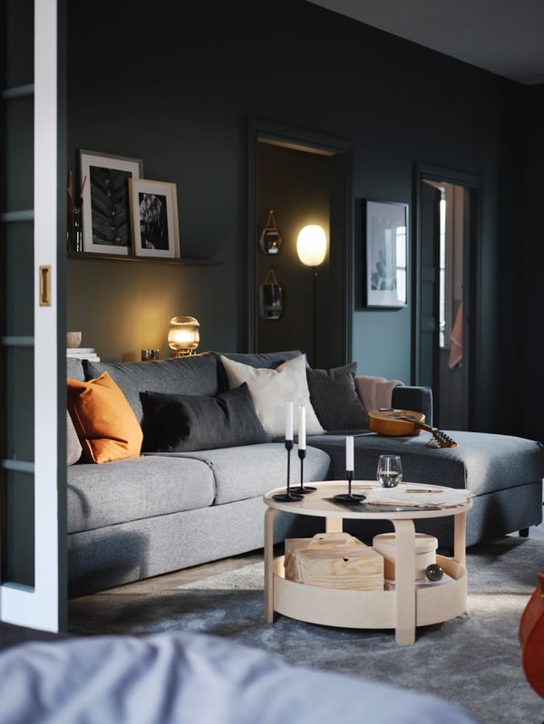 A grey VIMLE sofa with some colorful pillows in a dark green living room