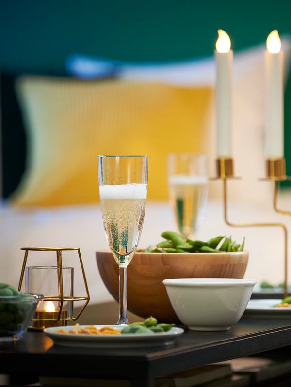 Sex SVALKA champagneglas på mässingsfärgade underlägg bredvid en mässingsfärgad bricka på ett bord med en vit duk.