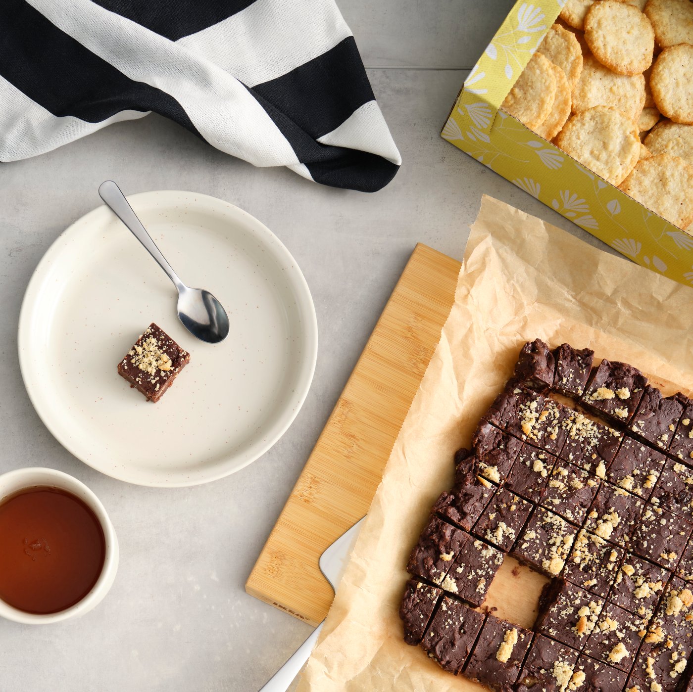 A kitchen counter with brown BJÄLLRA oat biscuits neatly arranged on the of a batch of chocolate fudge and a cup of tea.