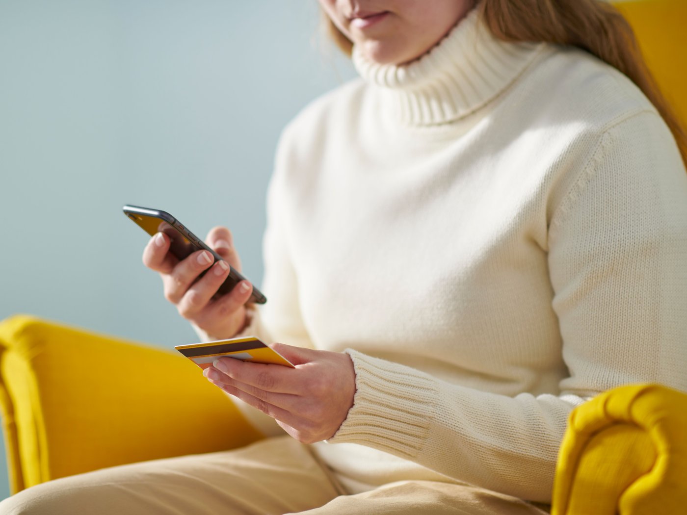 A woman sitting in a yellow IKEA chair holding her mobile device.