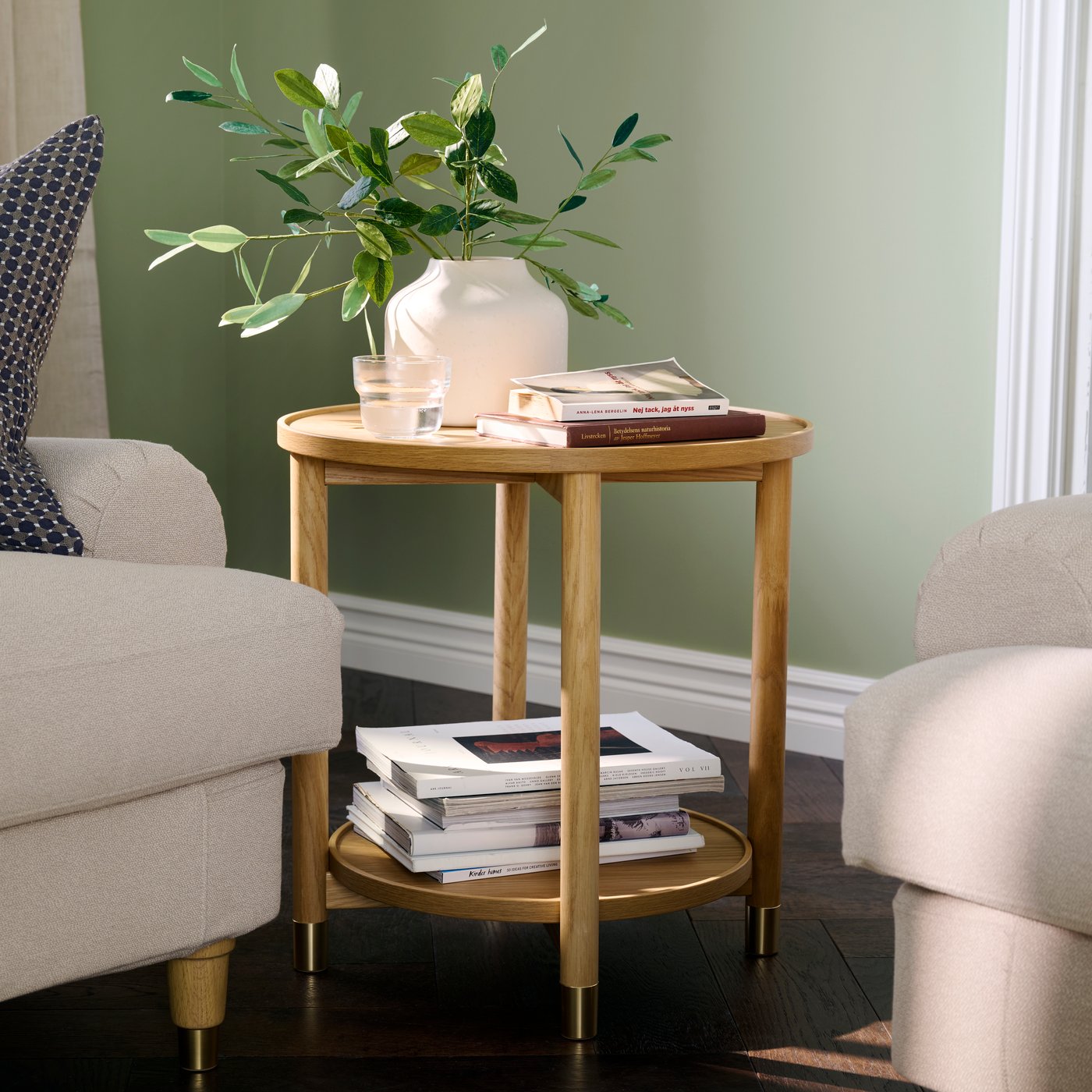 A living room with an oak veneer VALNÄS side table beside a beige armchair and stacked books.