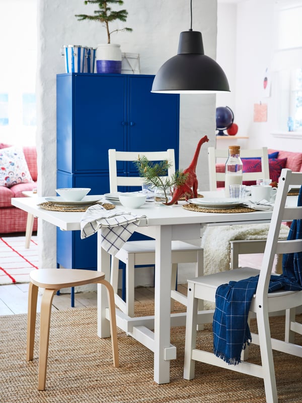 A white dining room containing an IDANÄS glass-door cabinet, and an INGATORP table with white and rattan chairs around it.