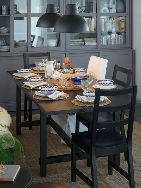 Mesa de comedor negra NORDVIKEN con sillas negras NORDVIKEN con individuales de bambú y platos blancos sobre ella.
