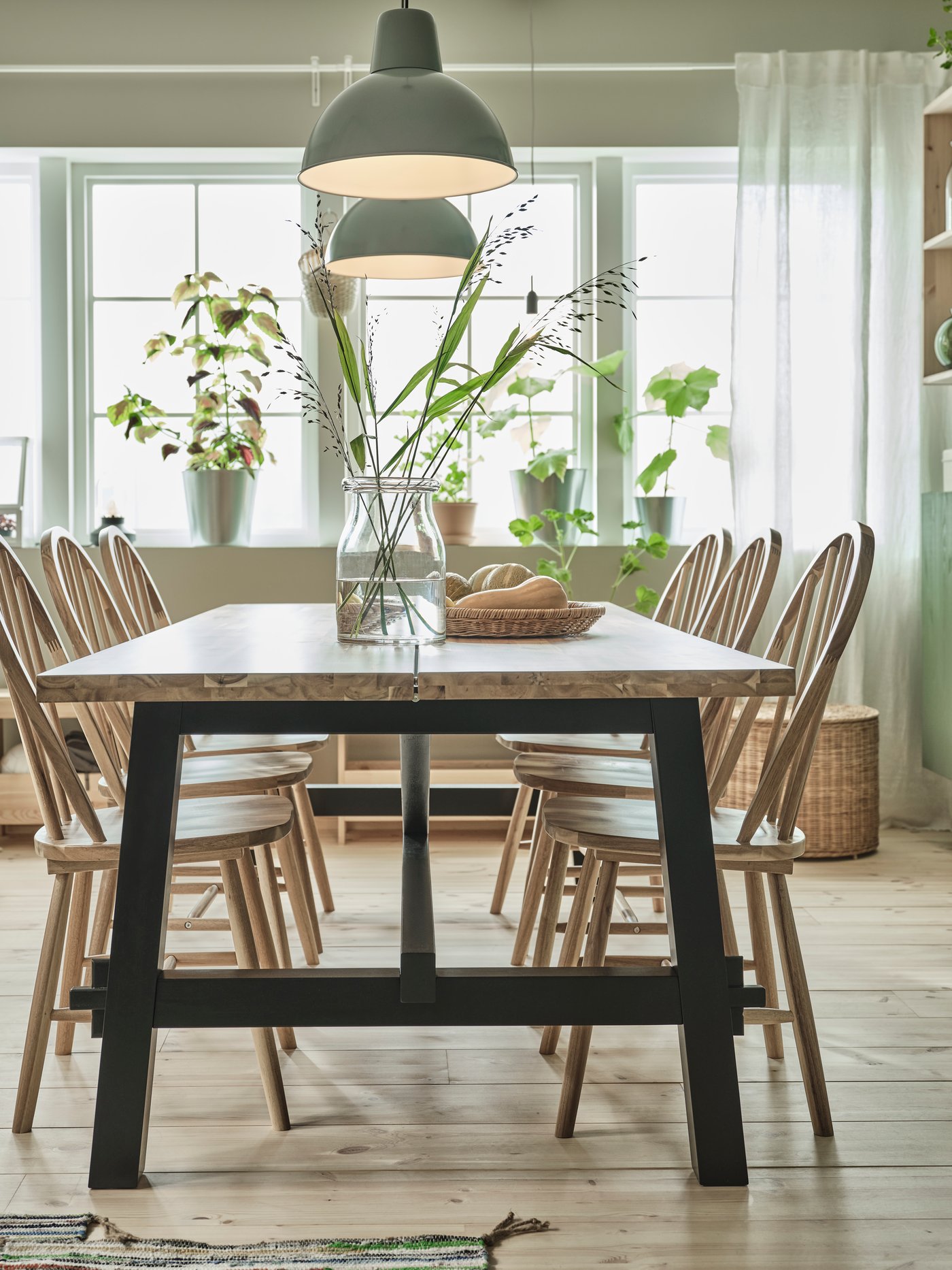 A wooden SKOGSTA dining table and six SKOGSTA chairs stand in a dining room under two SKURUP pendant lamps.