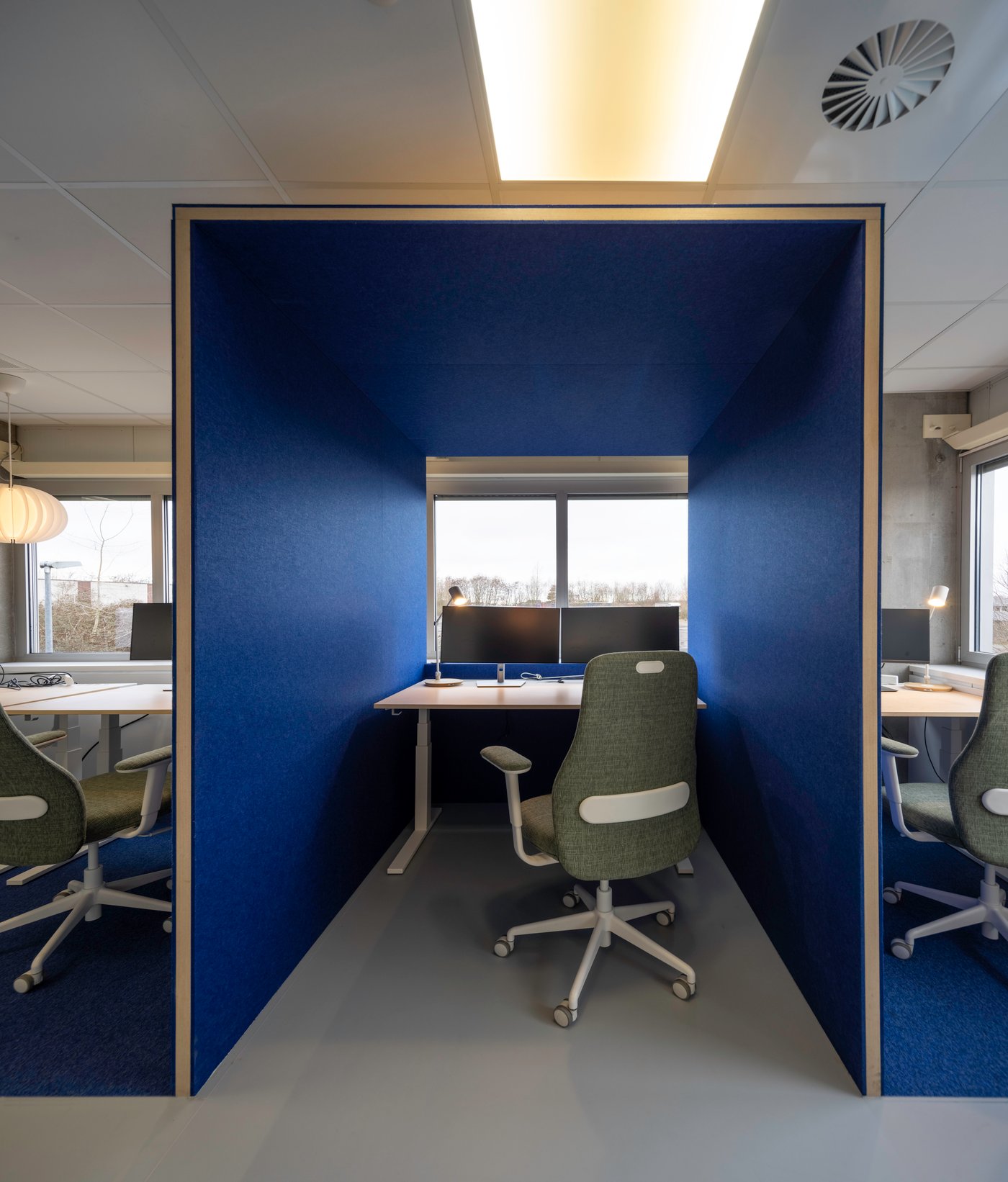Une niche bleue compacte avec des bureaux IKEA et des chaises ergonomiques offre un espace de travail calme entièrement dédié à la concentration.