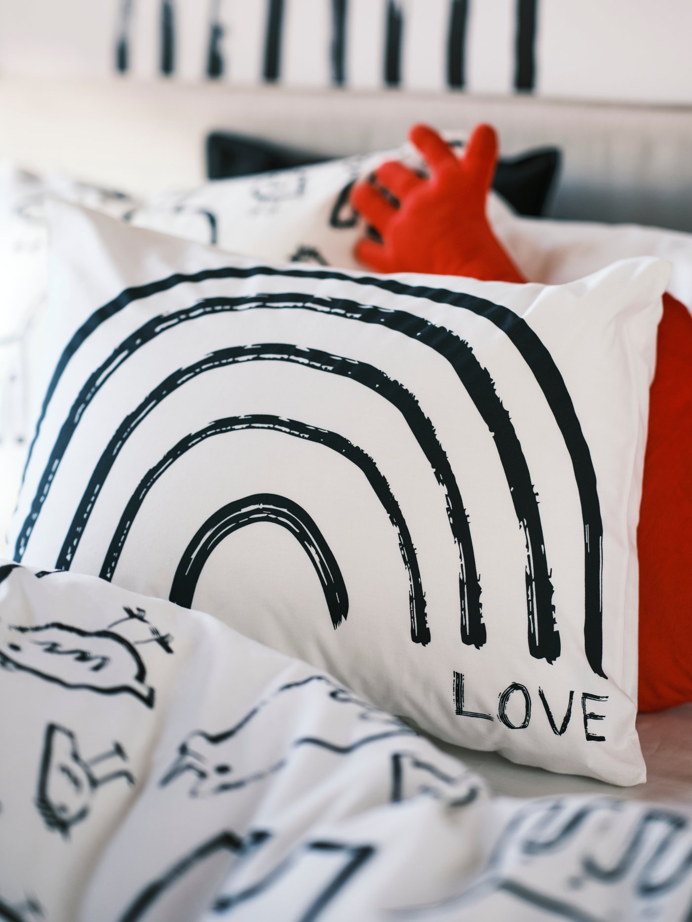 Kepala katil dilitupi linen katil PURPURBRÄCKA dengan bantal di dalam sarung bantal TAPETMAL dan kusyen berbentuk hati di atasnya.