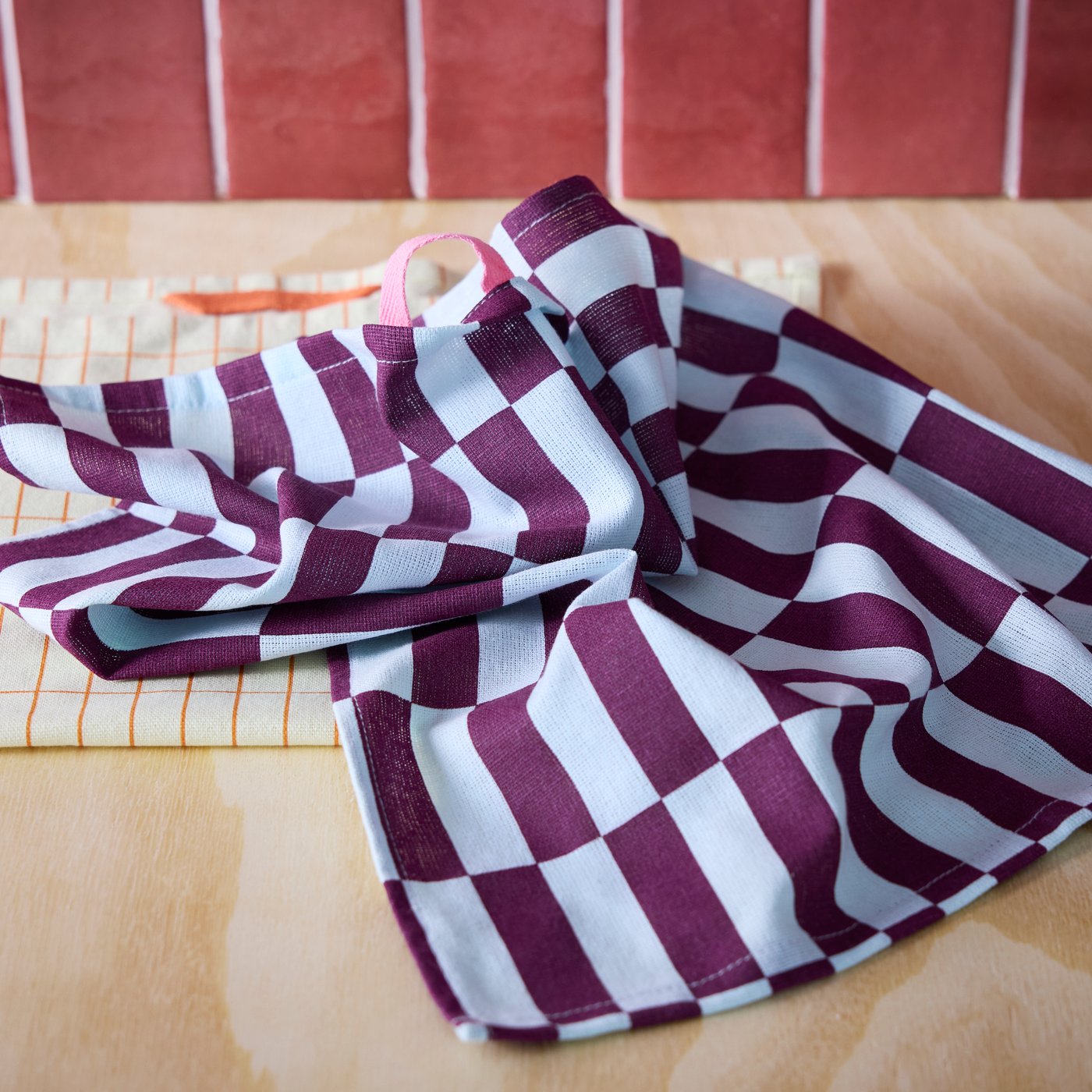 A SPJUTLILJA tea towel with a pattern of coloured rectangles lies on top of a SPJUTLILJA tea towel with a grid pattern.