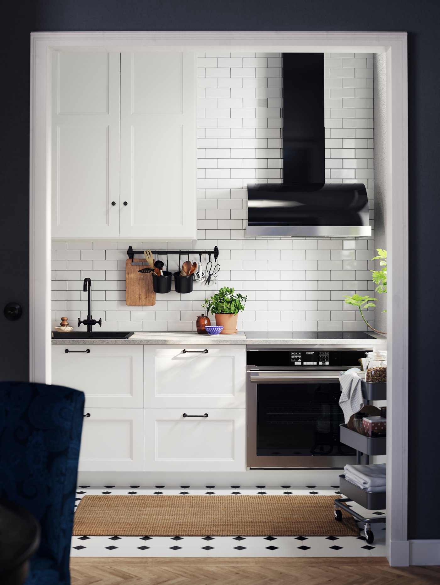 A kitchen with AXSTAD matte white kitchen fronts with black handles, a black tap, a trolley, against a tiled wall.