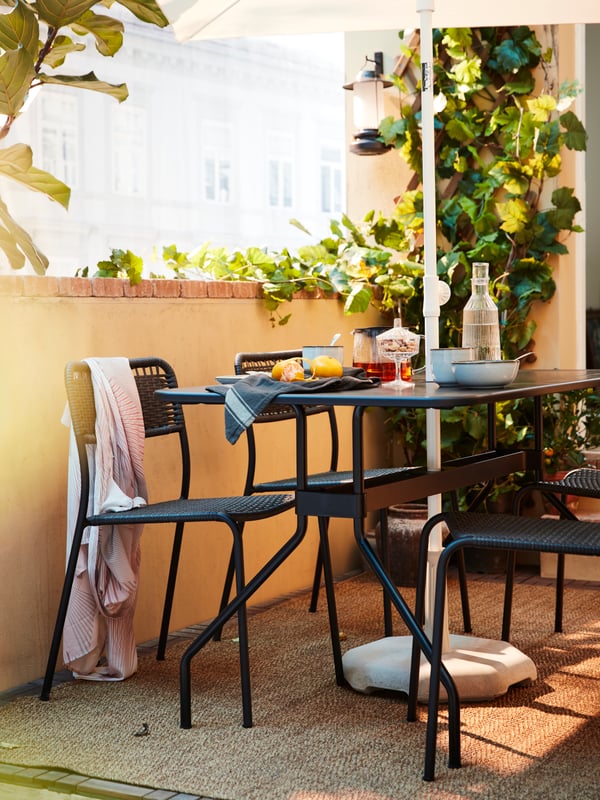 Un set di tavolo e sedie da esterno grigio scuro con frutta, tè, acqua e stoviglie su un terrazzo - IKEA