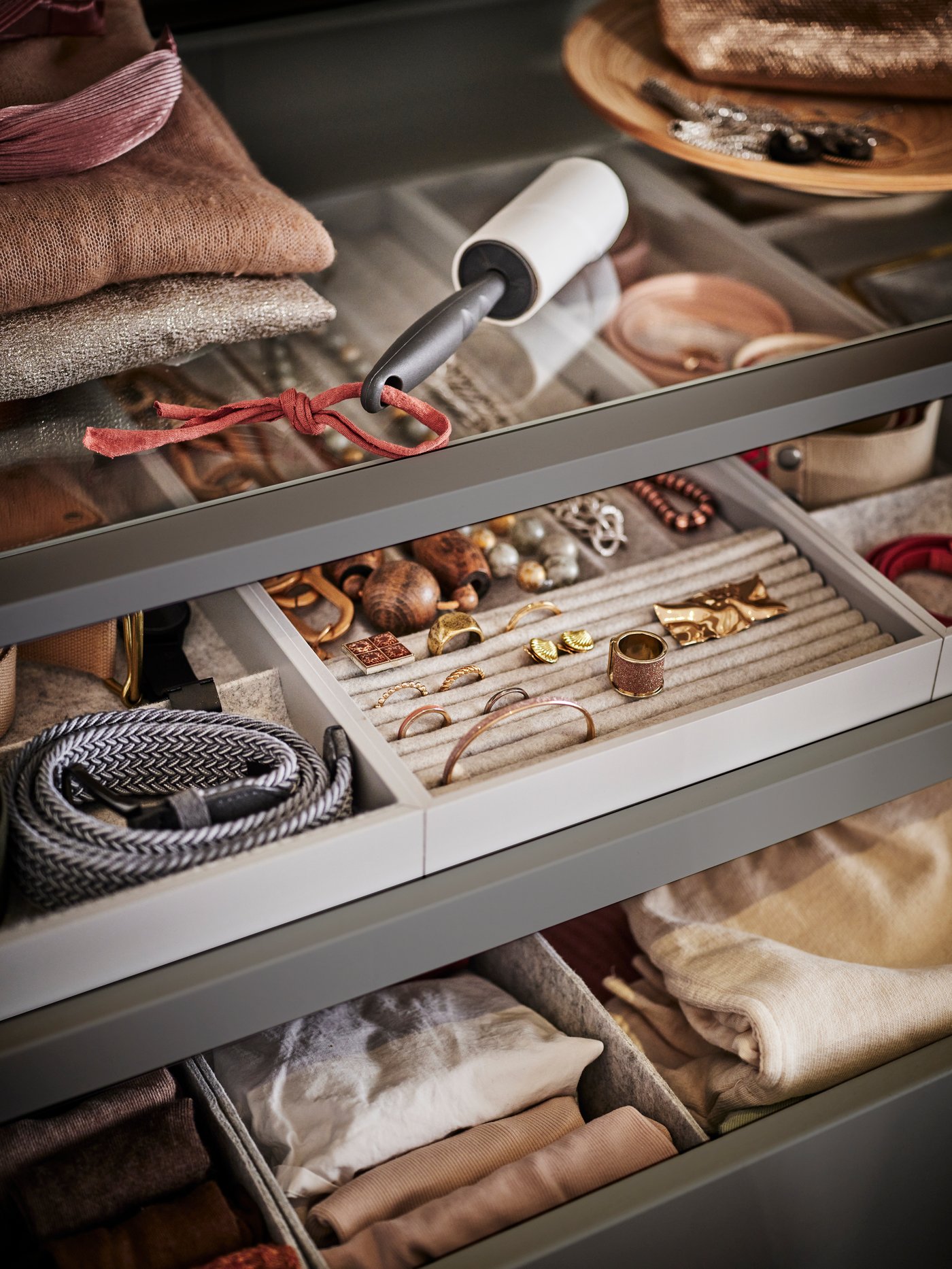 Two KOMPLEMENT pull-out drawers with inserts for storing accessories such as jewellery and belts. There is a lint roller on a shelf above.