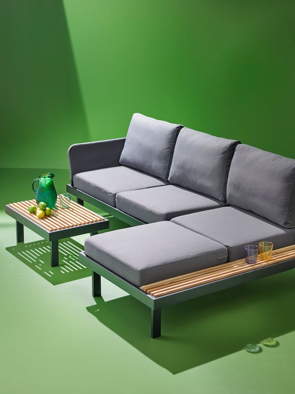 A REVSKÄR 3-seat conversation set, in anthracite, in a green space. There is a green jug, glass and limes on the side table.