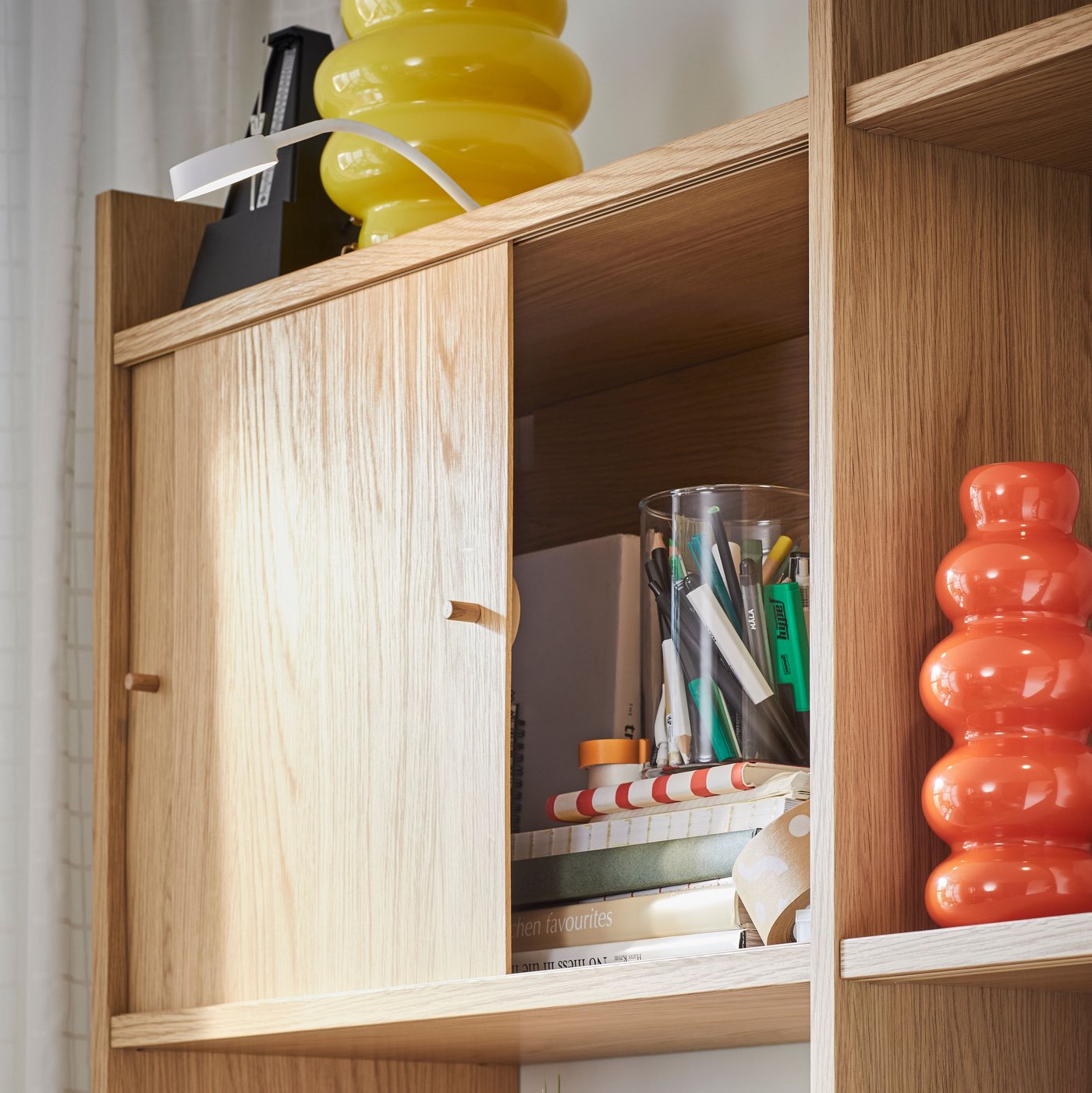 Del af en LÅDMAKARE opbevaringskombination med to skydedøre, der kan åbnes, og med en orange KÄLLARHALS vase på en hylde.