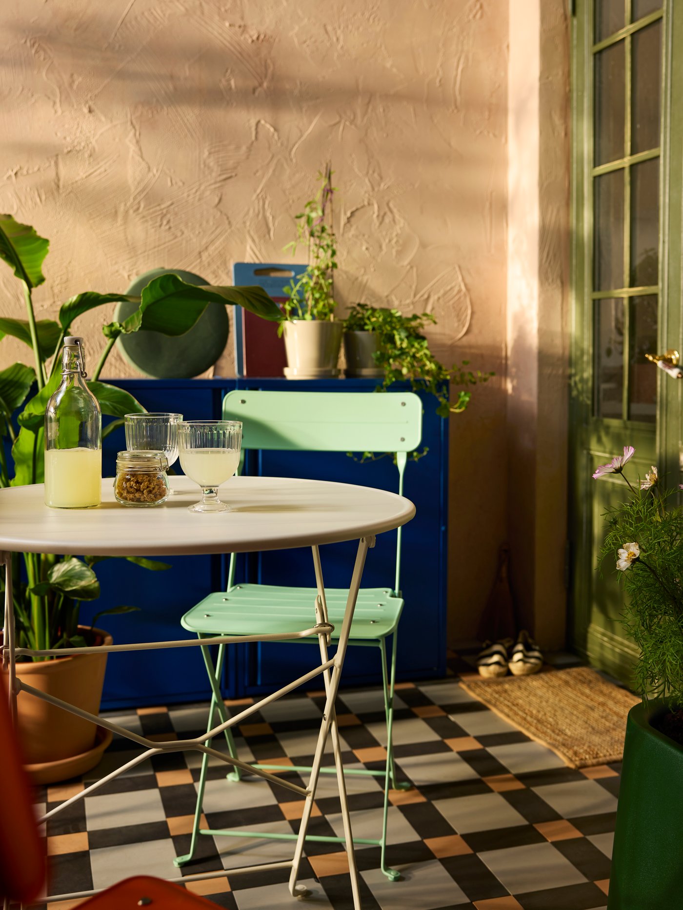 A balcony with a SUNDSÖ outdoor table and a light green SUNDSÖ folding chair and plants sitting on two SUNDSÖ cabinets.
