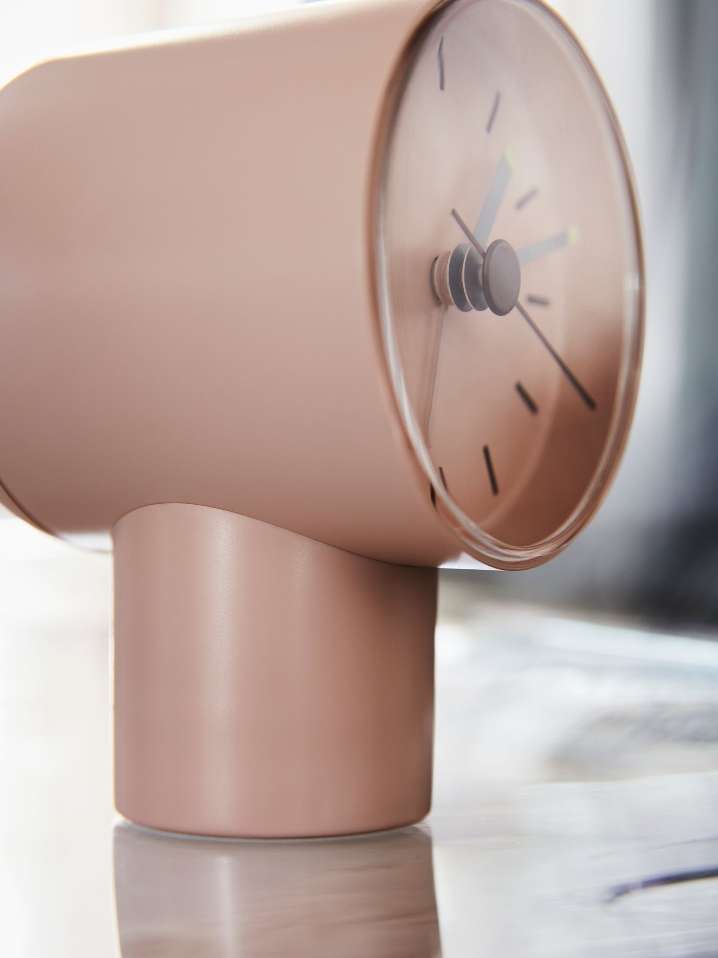 A light, dimly sunlit surface on which stands a pale-pink BONDTOLVAN analog alarm clock.