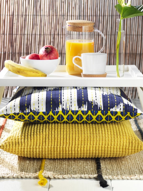 Three cushions with different covers are stacked on top of each other on an ALSEDA stool near a window with a curtain.