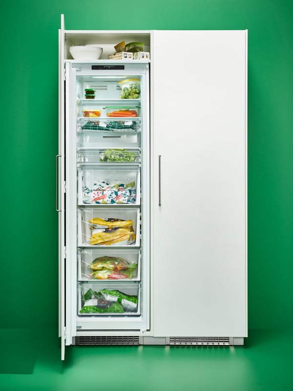 An opened FORSNÄS integrated freezer filled with various food items in a space with green walls and floors.