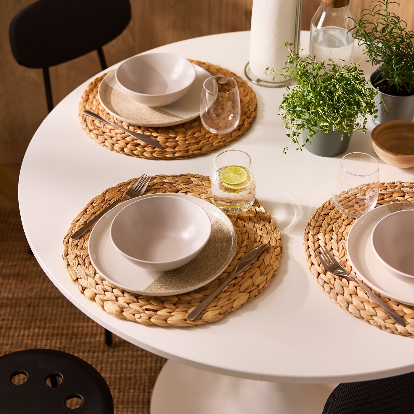 En solbelyst matplats med ett vitt, runt DOCKSTA-bord dukat med krukväxter och porslin på runda SOARÉ-placemats.