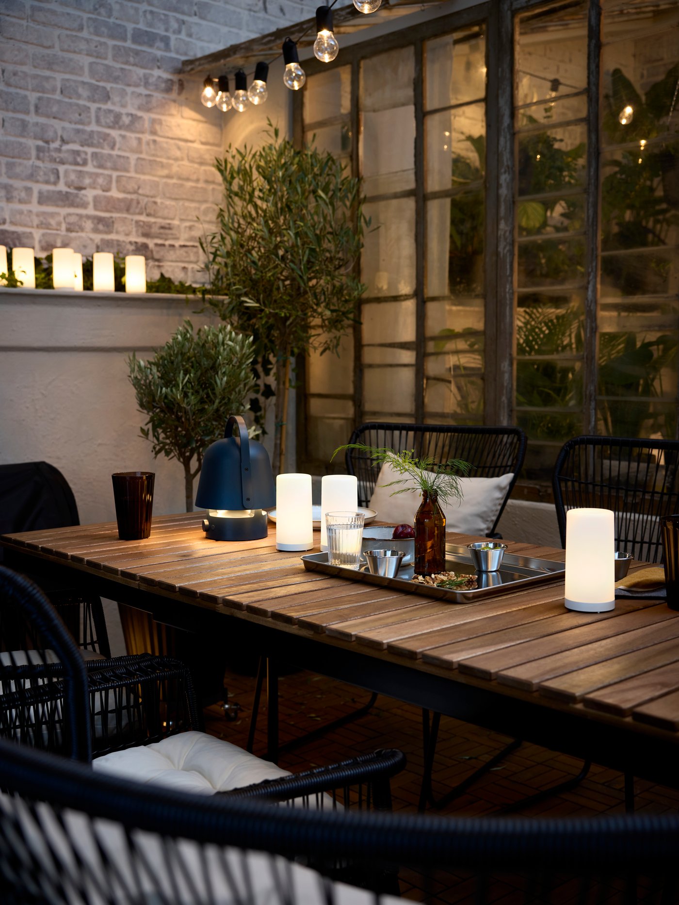 Table d’extérieur extensible VÄSMAN sur laquelle sont posées une décoration électrique à LED SOLVINDEN et une lampe enceinte Bluetooth VAPPEBY en bleu.