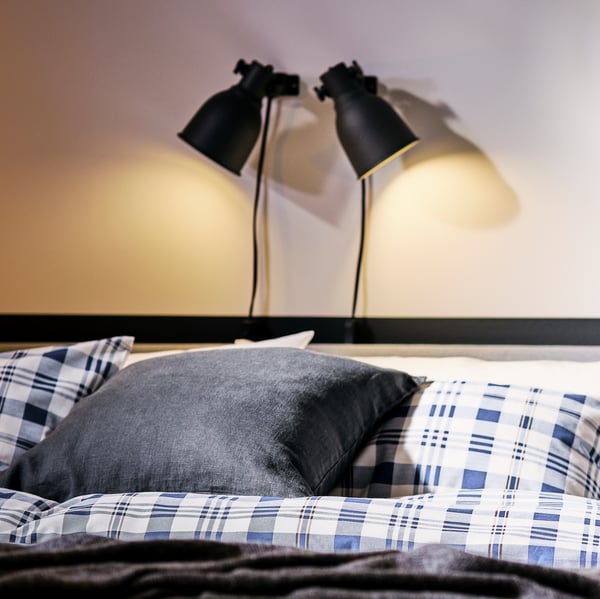 La tête d’un lit SLATTUM gris pâle avec du linge de lit SPIKVALLMO, éclairé par deux spots HEKTAR gris foncé.