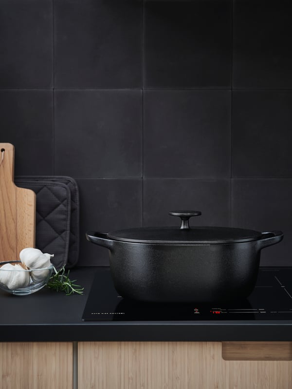 A VARDAGEN cast iron five quart casserole on a cooktop in a kitchen with a dark-gray countertop and matching, dark wall tiles.