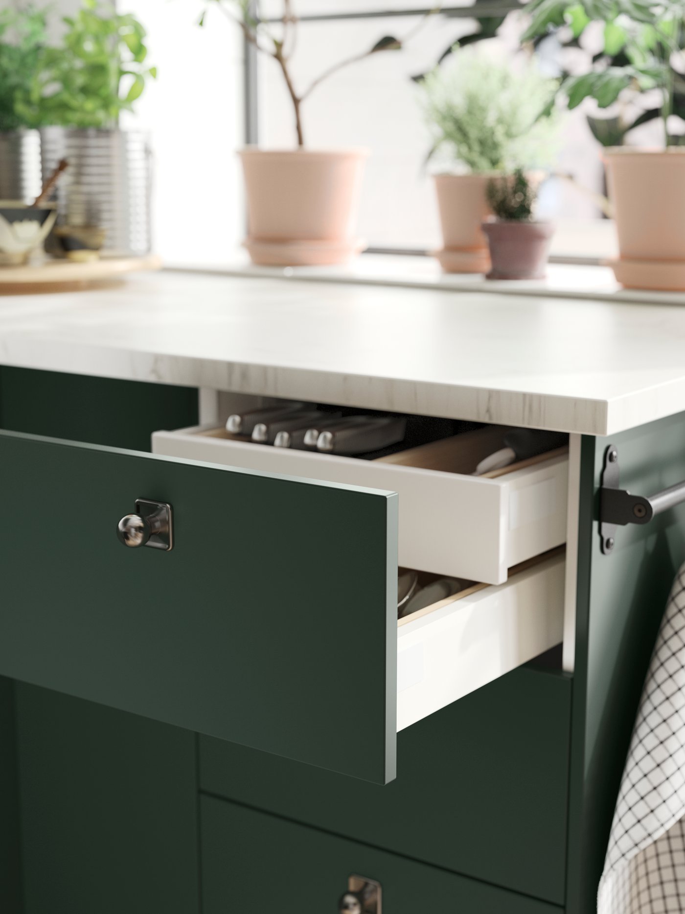 An open drawer in a kitchen with deep green HAVSTORP kitchen fronts and an inner drawer, both holding various items.
