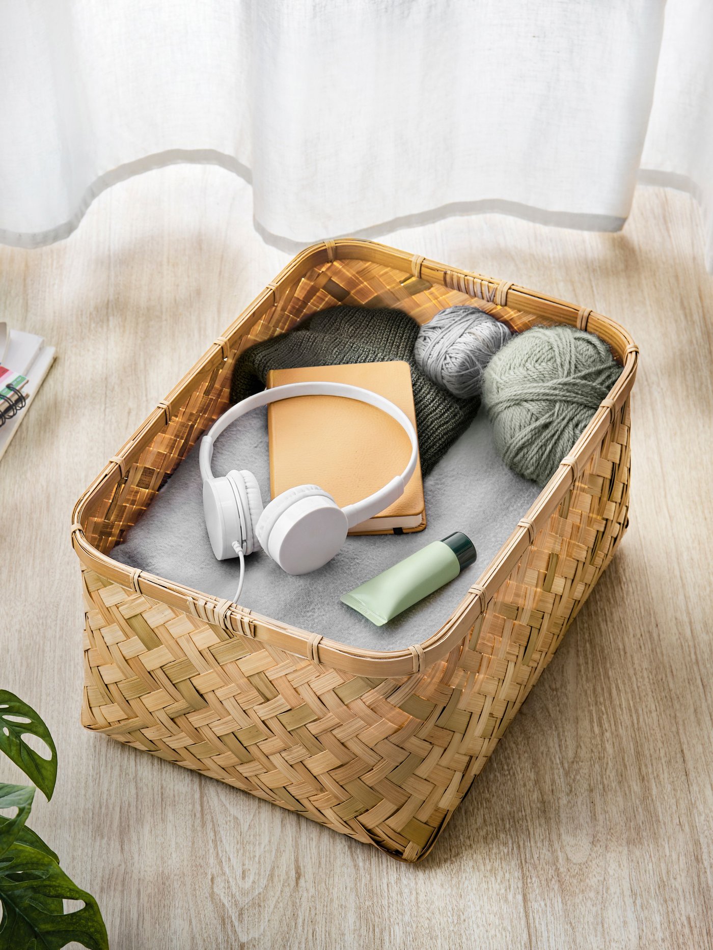 En kurv fyldt med et headset grå garn og en tube creme over kurven vajer et hvidt gardin.
