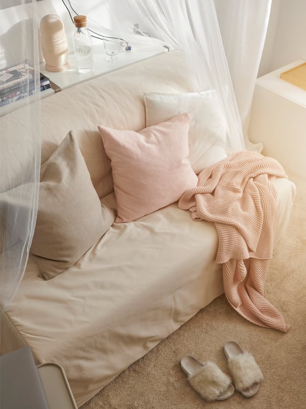 Tri jastučića na LYCKSELE HÅVET sofa ležaju. Preko njega je prebačeno roze tanko ćebe. Tanka tkanina okružuje sofa ležaj.