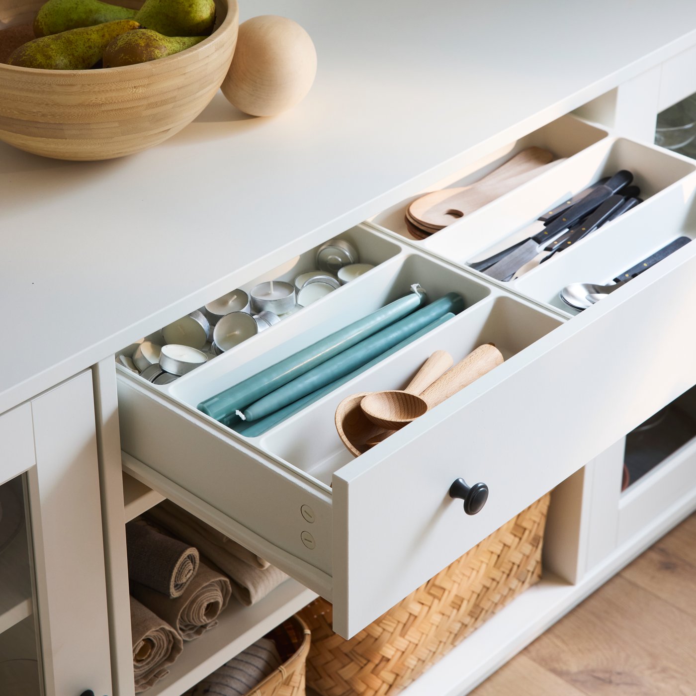 A drawer in a HAUGA sideboard is open and inside it there are two UPPDATERA cutlery trays with cutlery and candles in them.
