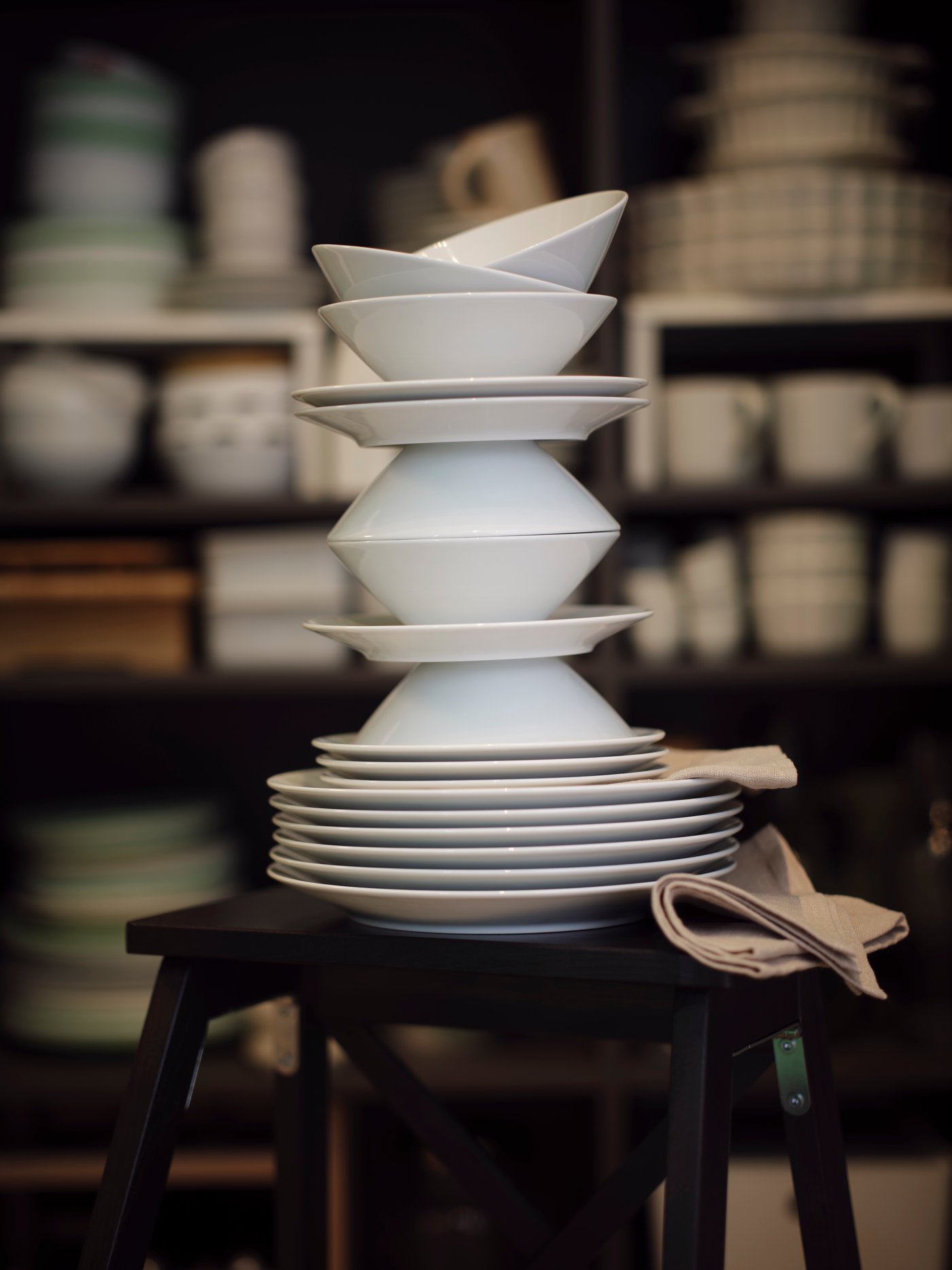 All pieces of a white IKEA 365+ 18-piece service are playfully stacked on top of each other on a black stepladder.