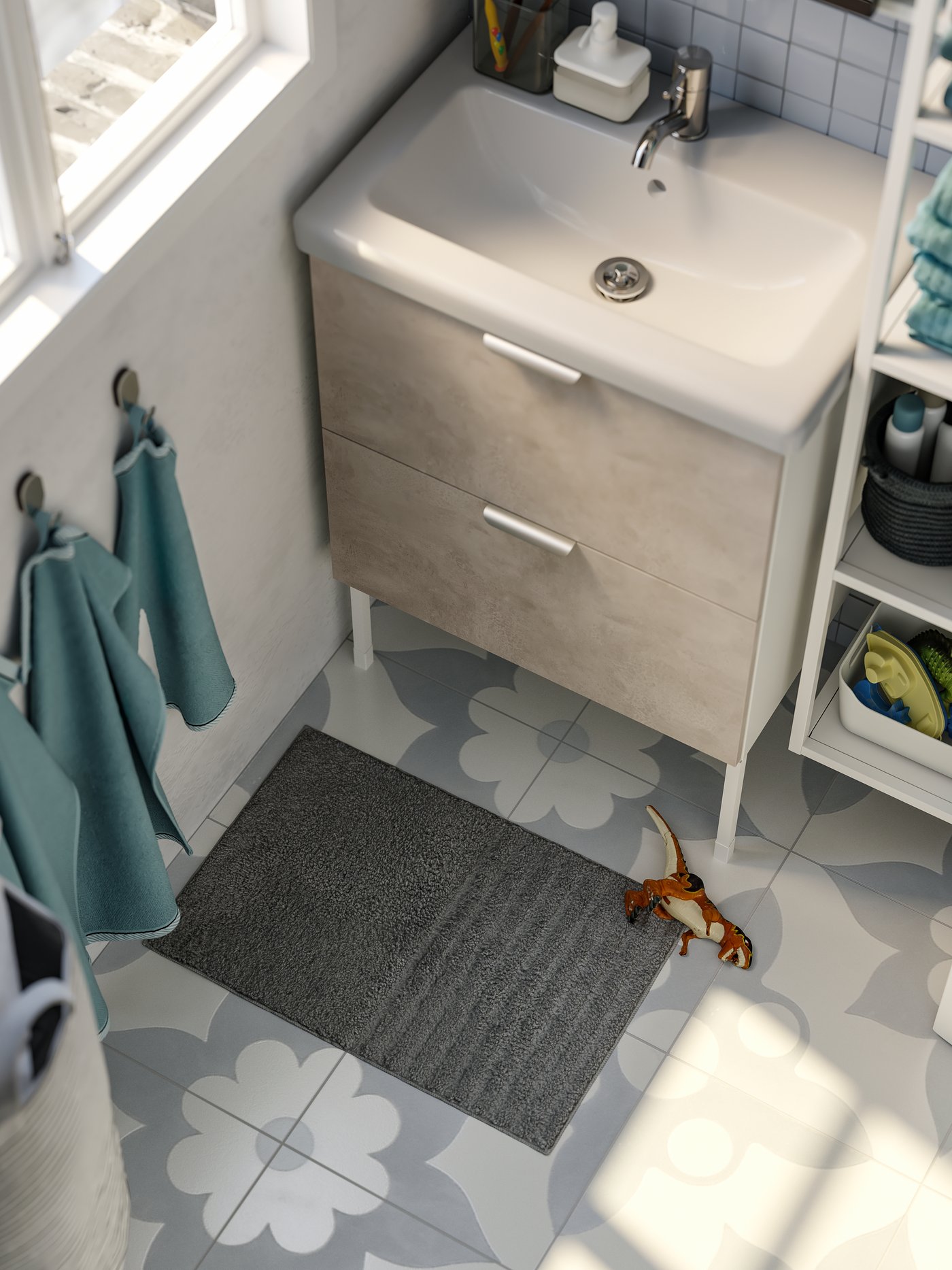 A grey bath mat with a dinosaur toy lying beside it, light blue towels hung on hooks on the wall, a white washbasin.