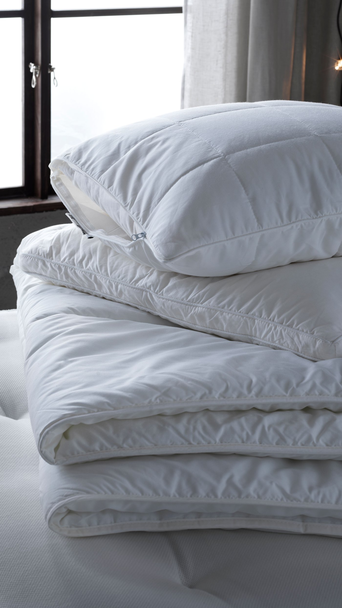 Un plumón cálido STJÄRNBRÄCKA sobre una cama con una almohada blanca.