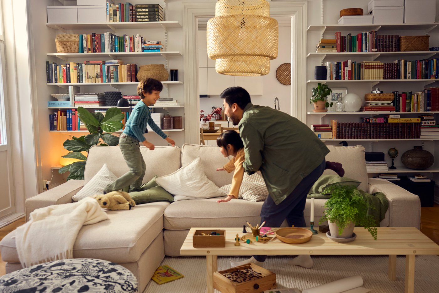 A father is playing with his two children in a bright living room.