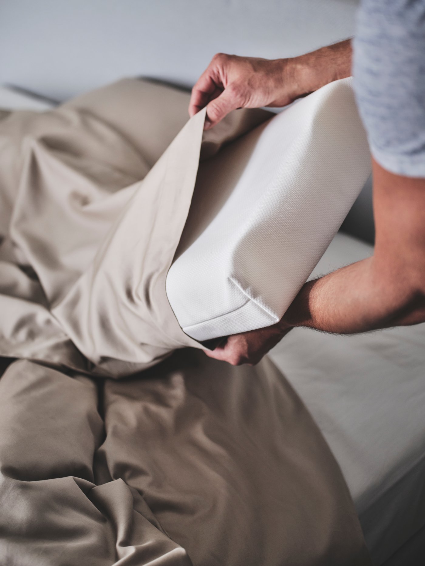 Un hombre poniendo una almohada PAPEGOJBU en una funda de almohada LUKTJASMIN.