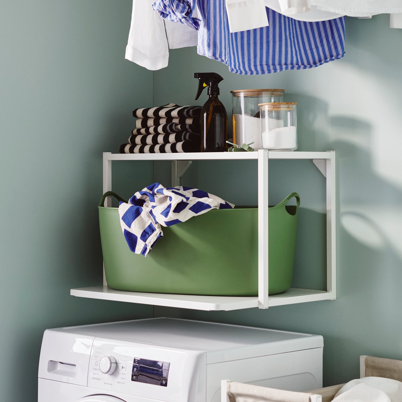 Système d'étagères ENHET blanc au-dessus d'une machine à laver, avec panier à linge, serviettes et bocaux. Solution IKEA pratique.