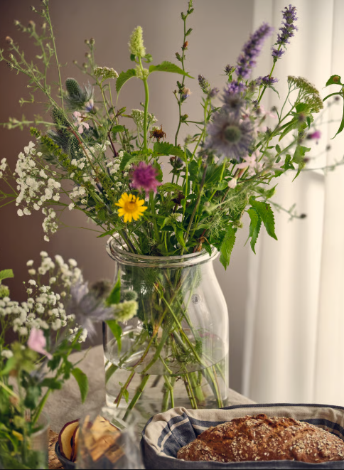 Vase mit bunten Wildblumen auf einem Tisch, daneben ein Teller mit Gebäck in heller, natürlicher Umgebung.
