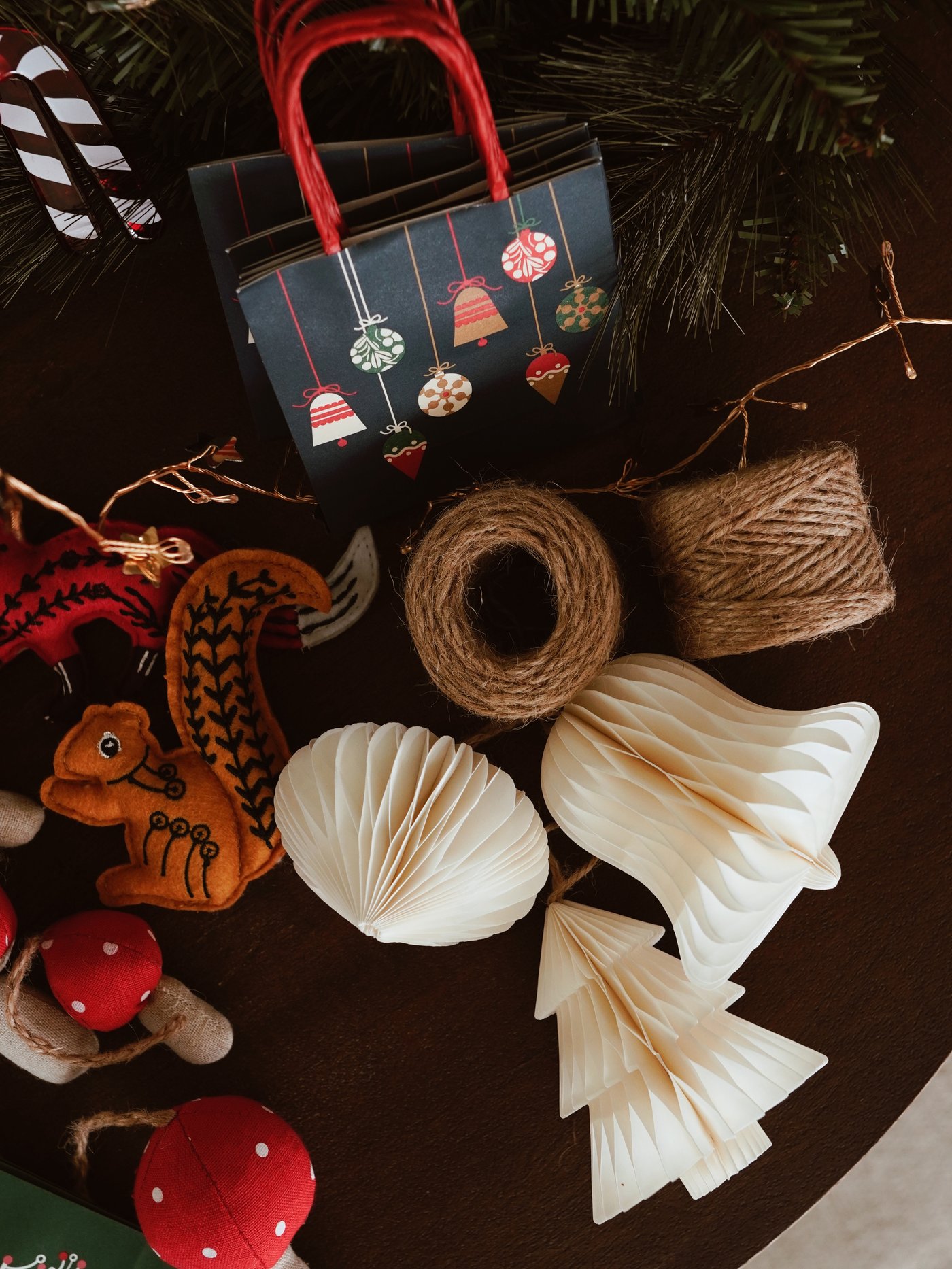 Eine festliche Tischdekoration mit Papierornamenten, Tannenzapfen, einer Garnrolle und Filzdekorationen neben einer dunklen Geschenktüte mit festlichen Motiven.