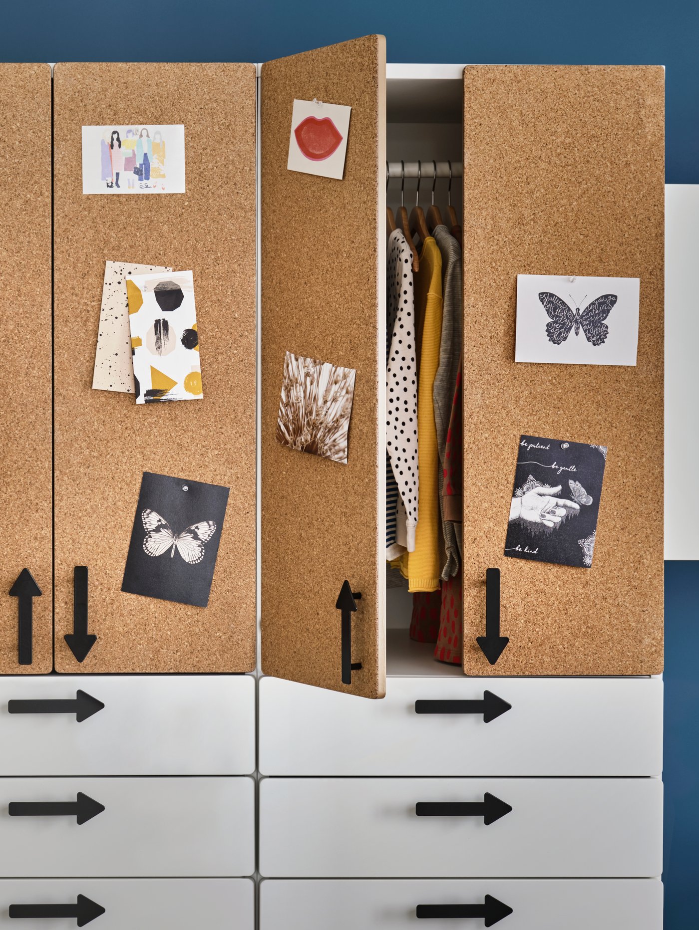 Two SMÅSTAD wardrobes with white drawers, cork doors and arrow-shaped handles stand next to each other. One has an open door.