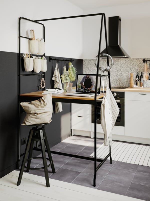 A black HÅVERUD table with bags hanging from the ladder storage on one side and a tea towel and headphone on the other side.