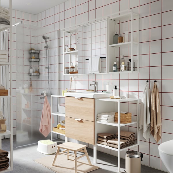 Meuble-lavabo ENHET en bois naturel et blanc avec des accessoires noirs dans une salle de bains lumineuse en blanc et beige.