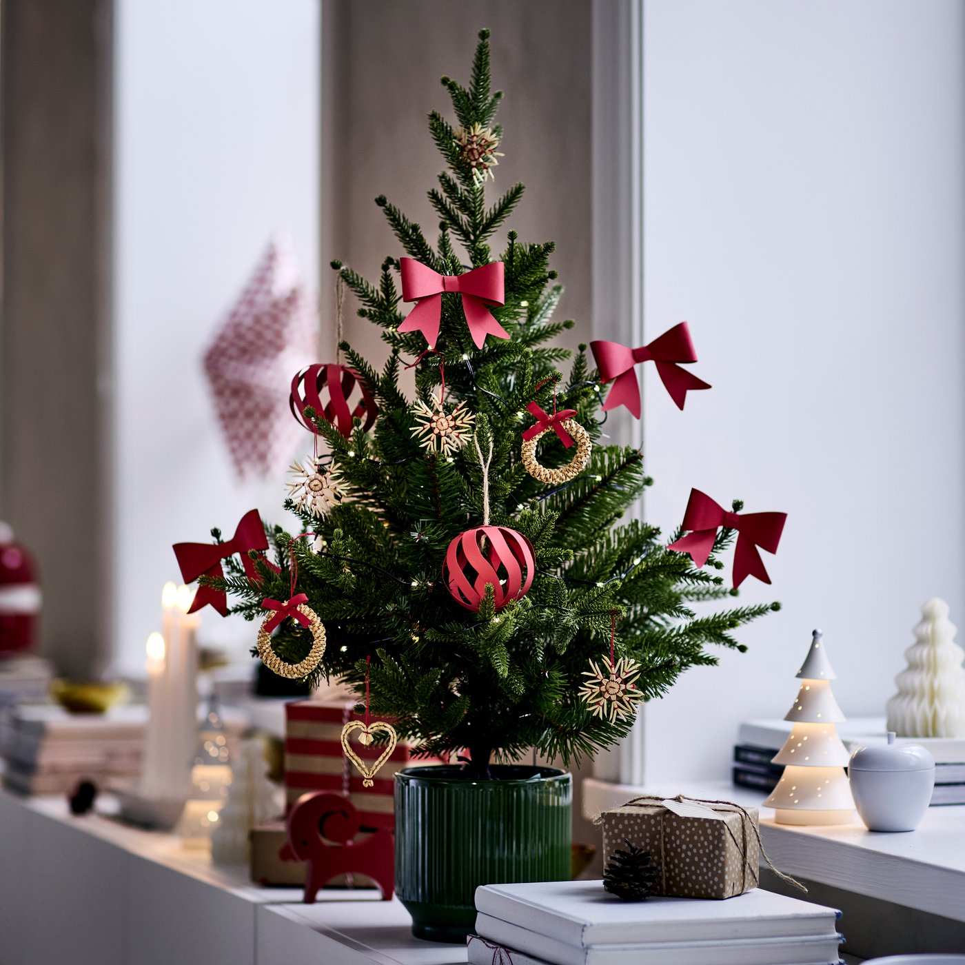 A small potted tree is decorated with red and gold VINTERFINT tree ornaments and is placed on a sideboard.