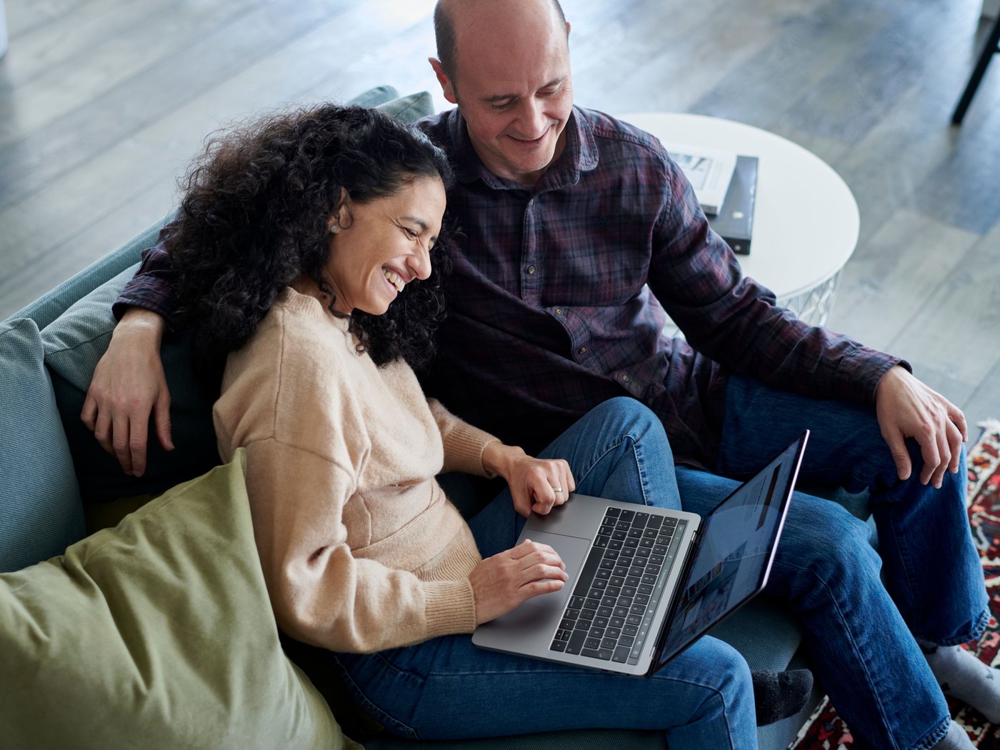 A man and a woman is seen sitting in a couch with a laptop in front of them