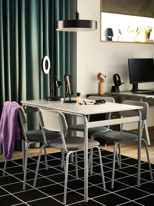 A grey GRÅSALA dining set with four chairs in a small studio apartment with beauty products on the table top.