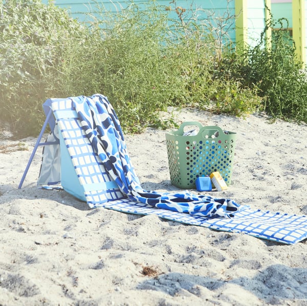STRANDÖN sun lounger in blue and white set up on the beach with a towel on top, ready for you to relax and enjoy the sunshine.