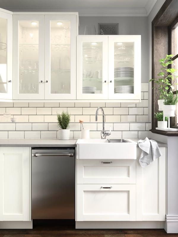 A SEKTION kitchen with white tiled walls and ENKÖPING kitchen fronts in white and white wall cabinets and some green plants.