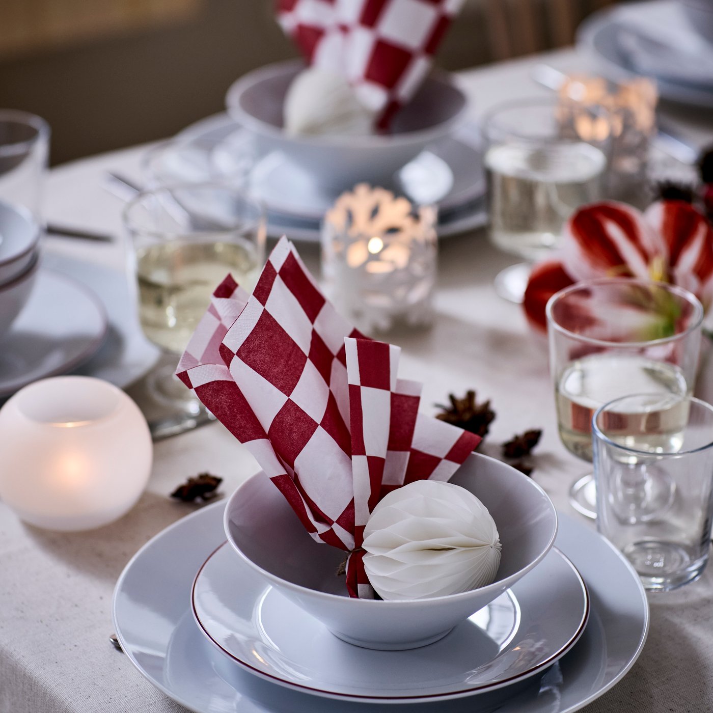 A red and white-checkered VINTERFINT paper napkin is playfully folded and set in a bowl, on a Christmas dinner table.