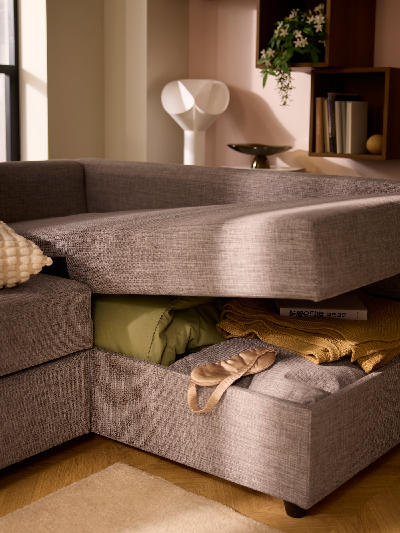 The gaping chaise-longue part of a FRIHETEN sofa-bed, revealing bedding and textiles placed in the compartment within.