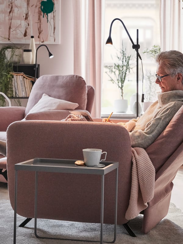 Una donna è comodamente seduta su una poltrona reclinabile EKOLSUND con fodera GUNNARED marrone chiaro-rosa accanto a un tavolino - IKEA